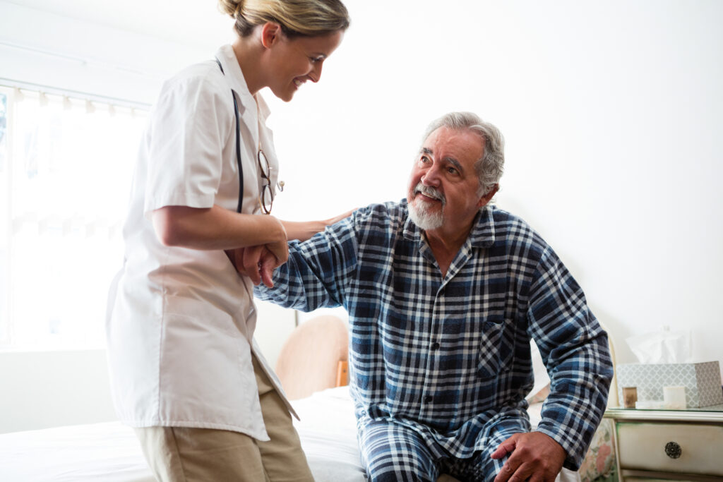 Female doctor assisting senior man in sitting on bed