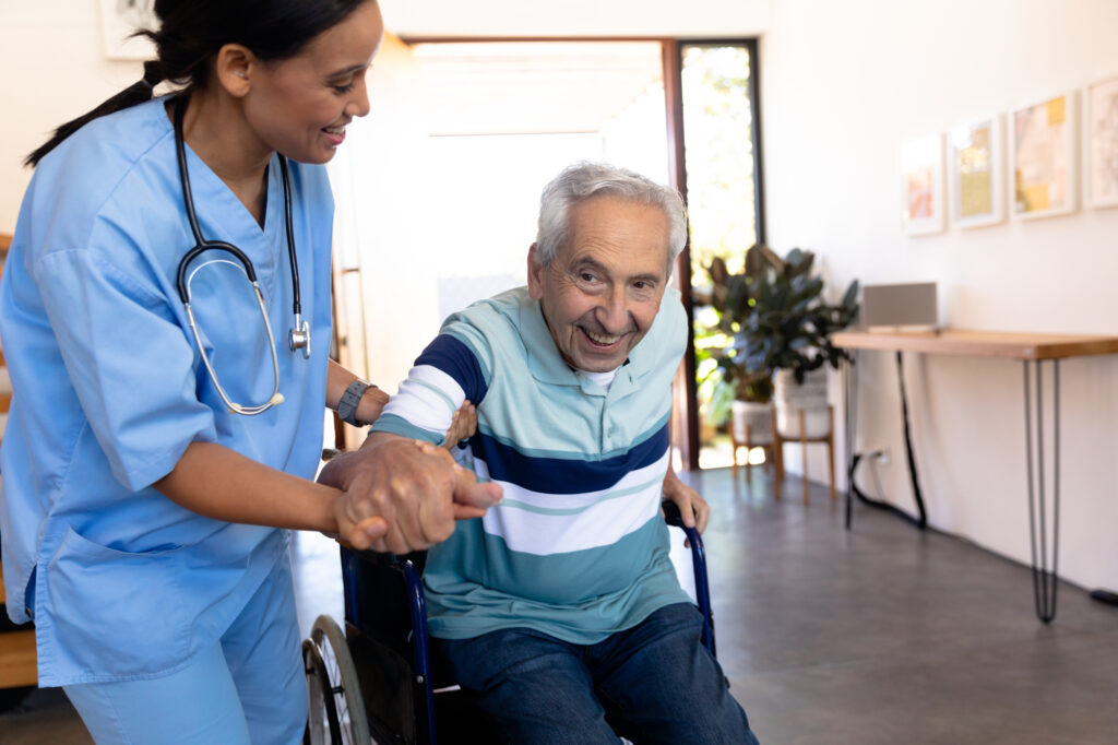 Biracial female physiotherapist assisting smiling caucasian senior man in getting up from wheelchair. Home, unaltered, physical impairment, retirement, support, healthcare, recovery and disability.